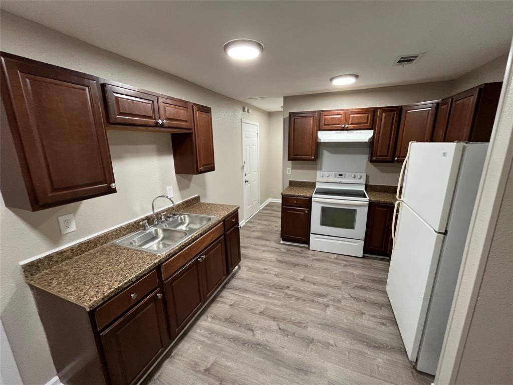 Kitchen featuring dark wood-finish cabinetry, stone-finish laminate countertops, dual-basin stainless steel sink, and wood-finish flooring