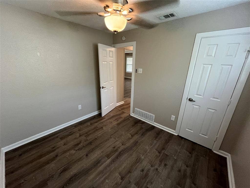 Room featuring wood-finish flooring, six-panel interior doors, and a ceiling-mounted light fixture with a fan