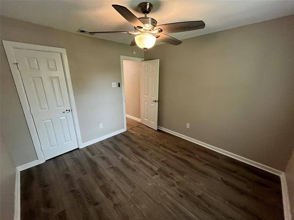 Room featuring wood-finish flooring, a multi-blade ceiling fan with integrated lighting, and two six-panel interior doors