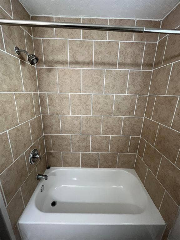Bathtub featuring a white acrylic finish, full-height tile surround, chrome faucet hardware, and a mounted showerhead