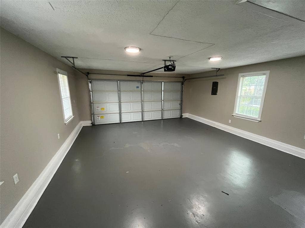 Two-car garage featuring painted concrete flooring, two windows with blinds, and ceiling-mounted lighting