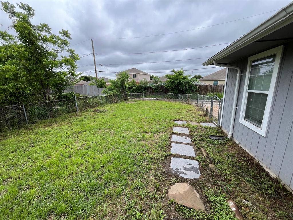 Backyard featuring a grass lawn, stone paver pathway, and chain-link fencing