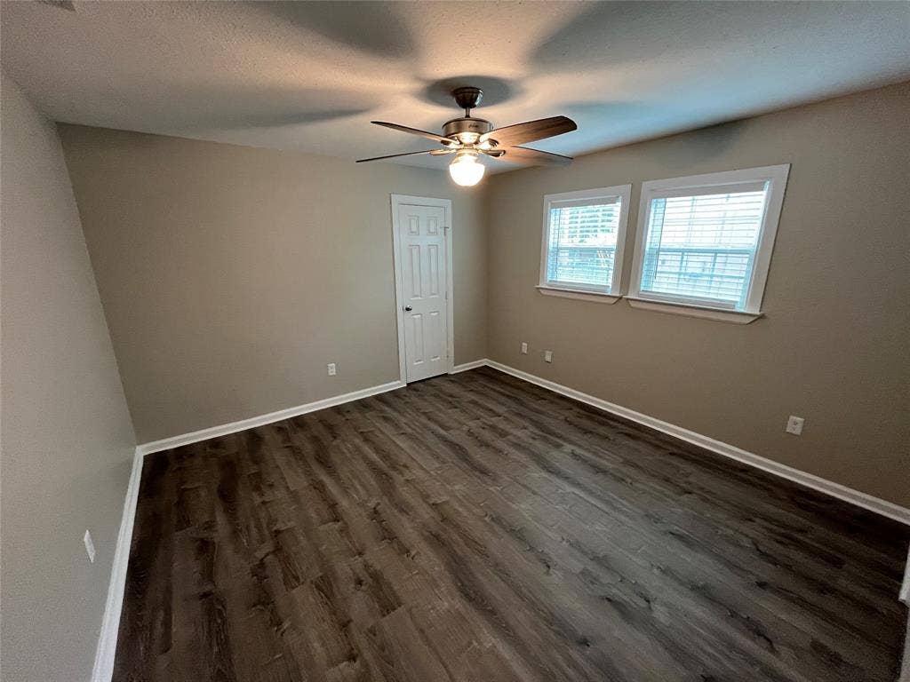Interior space featuring wood-finish flooring, dual windows with blinds, and a multi-blade ceiling fan with an integrated light fixture