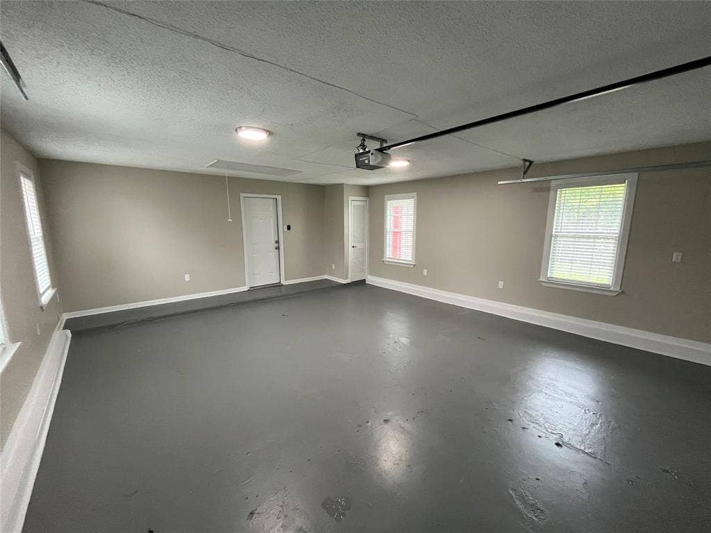 Finished interior space featuring painted concrete flooring, neutral wall tones, three multi-pane windows, and an overhead garage door opener