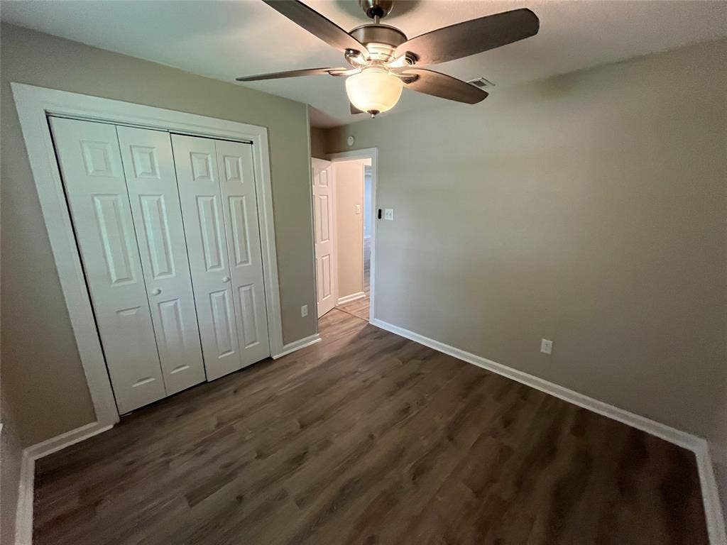 Neutral-toned room featuring wood-finish flooring, a multi-panel bi-fold closet, and a ceiling fan with integrated lighting