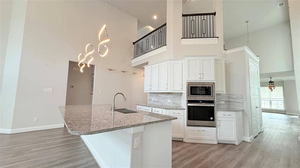 315 Chandan Way, Irving, TX 75063 Kitchen featuring high ceilings, white cabinetry, integrated stainless steel double wall ovens, a stone-surface island with a single-basin undermount sink, and wood-finish flooring