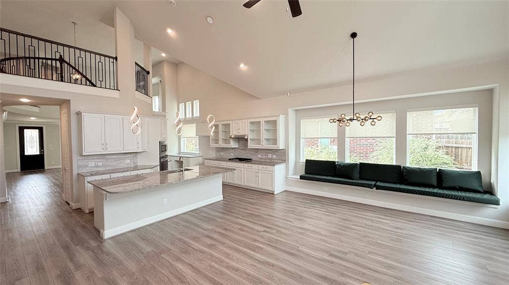 315 Chandan Way, Irving, TX 75063 Open-concept kitchen featuring an expansive quartz-topped island, white cabinetry with glass-front accents, wood-finish flooring, vaulted ceilings, and a built-in window bench