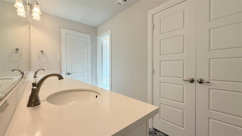 315 Chandan Way, Irving, TX 75063 Extended vanity featuring a solid-surface countertop with an integrated oval basin, polished metallic faucet hardware, a multi-bulb vanity light fixture, and classic five-panel interior doors