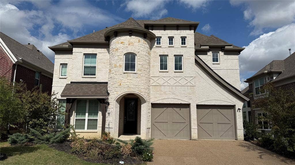 315 Chandan Way, Irving, TX 75063 Two-story exterior featuring light-toned brick and stone masonry, a prominent turret entry, decorative masonry detailing, and attached two-car garage with carriage-style doors