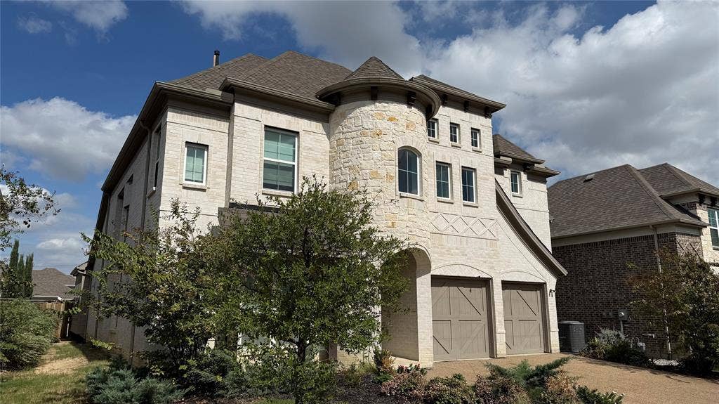 315 Chandan Way, Irving, TX 75063 Multi-story residence featuring light-toned brick facade, prominent stone turret, decorative cross-hatching masonry detail, and two-car garage with carriage-style doors