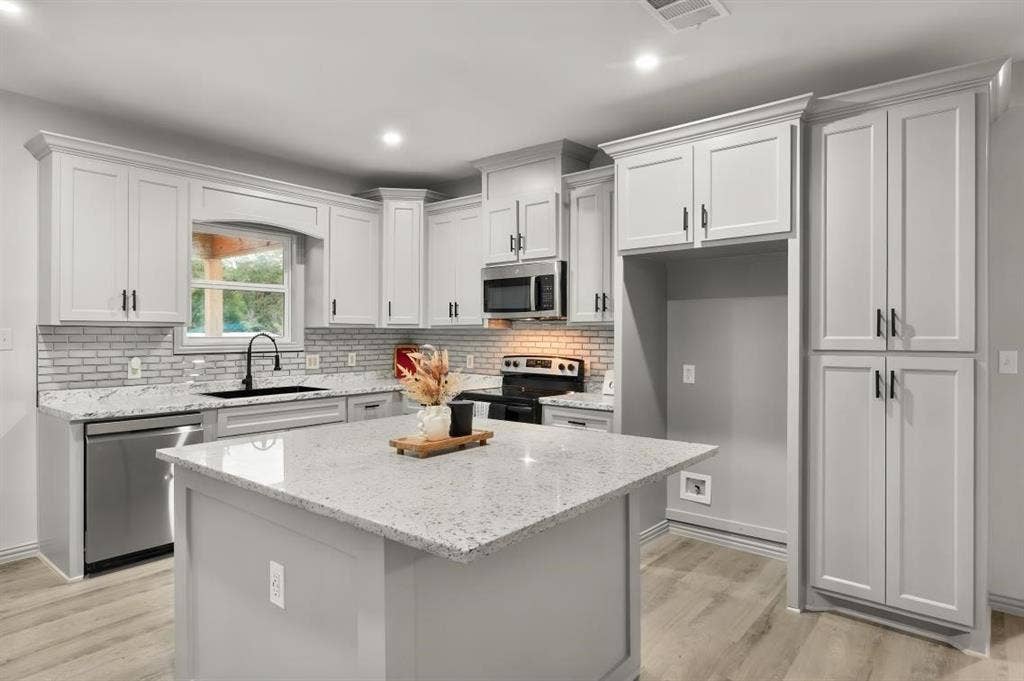 Kitchen featuring shaker-style cabinetry, a central island with a stone-finish countertop, stainless steel appliances, a light-toned brick-pattern backsplash, and wood-finish flooring