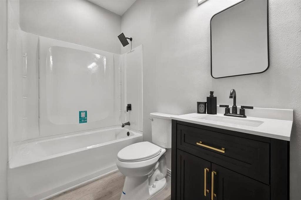 Bathroom featuring a dark wood-finish vanity with a light-colored countertop, matte black fixtures, integrated bathtub and shower surround, and a rectangular wall-mounted mirror