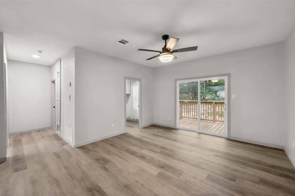 Neutral interior featuring wood-finish flooring, a contemporary ceiling fan with integrated lighting, and sliding glass doors leading to an exterior wood deck