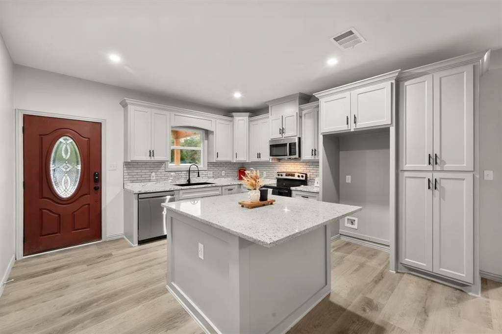 Kitchen featuring light-toned cabinetry, a central island with a stone-composite countertop, light wood-finish flooring, a tiled backsplash, and recessed lighting