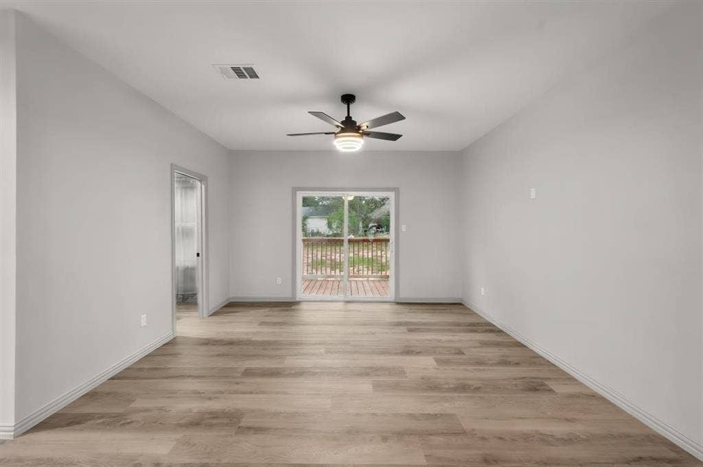 Neutral-toned interior featuring wood-finish flooring, a ceiling fan with integrated lighting, and a sliding glass door providing access to a deck