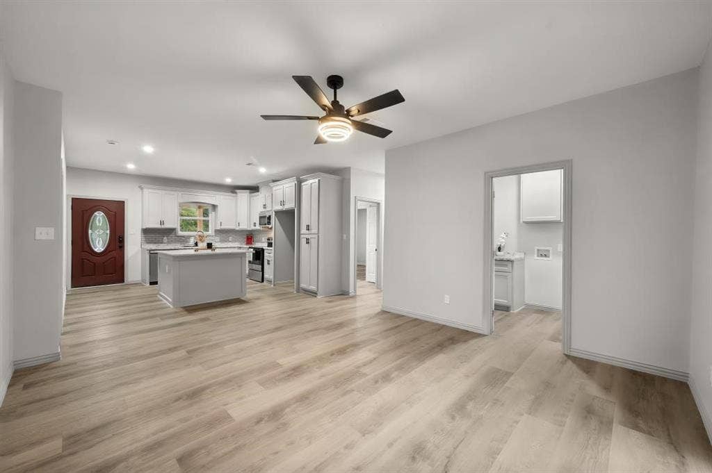 Open-concept interior featuring wood-finish flooring, a kitchen island, white cabinetry, and a ceiling fan with integrated lighting