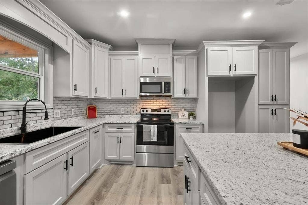 Kitchen featuring white shaker-style cabinetry, stone-finish countertops, subway tile backsplash, stainless steel appliances, and wood-finish flooring