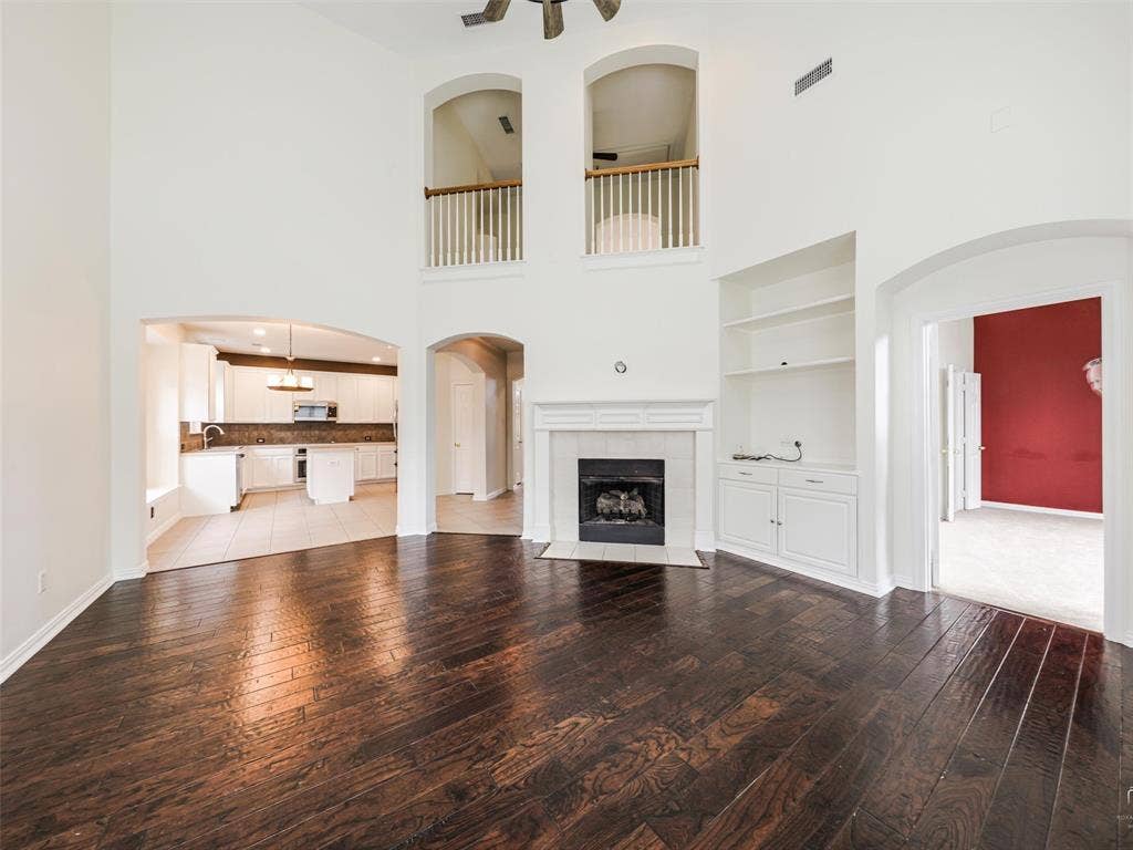 3504 Anita Drive, McKinney, TX 75070 Expansive living area featuring vaulted ceilings, wood-finish flooring, a fireplace with a custom mantle, built-in shelving, and architectural arched openings