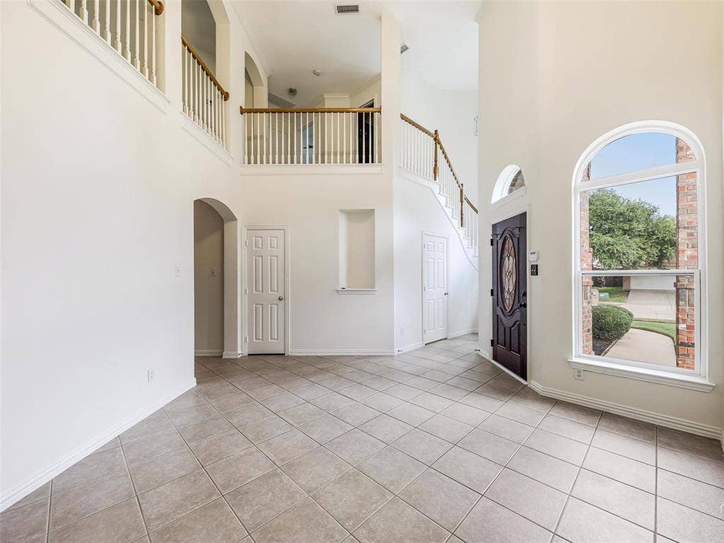 3504 Anita Drive, McKinney, TX 75070 Front room with two-story foyer featuring tile flooring, an arched window, a built-in recessed niche, and a wooden staircase with a railed balcony