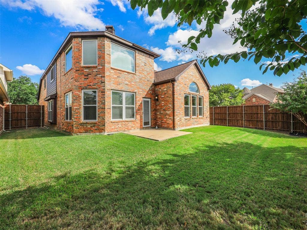 3504 Anita Drive, McKinney, TX 75070 Brick exterior featuring a multi-gabled roofline, expansive lawn, concrete patio, and perimeter wood fencing