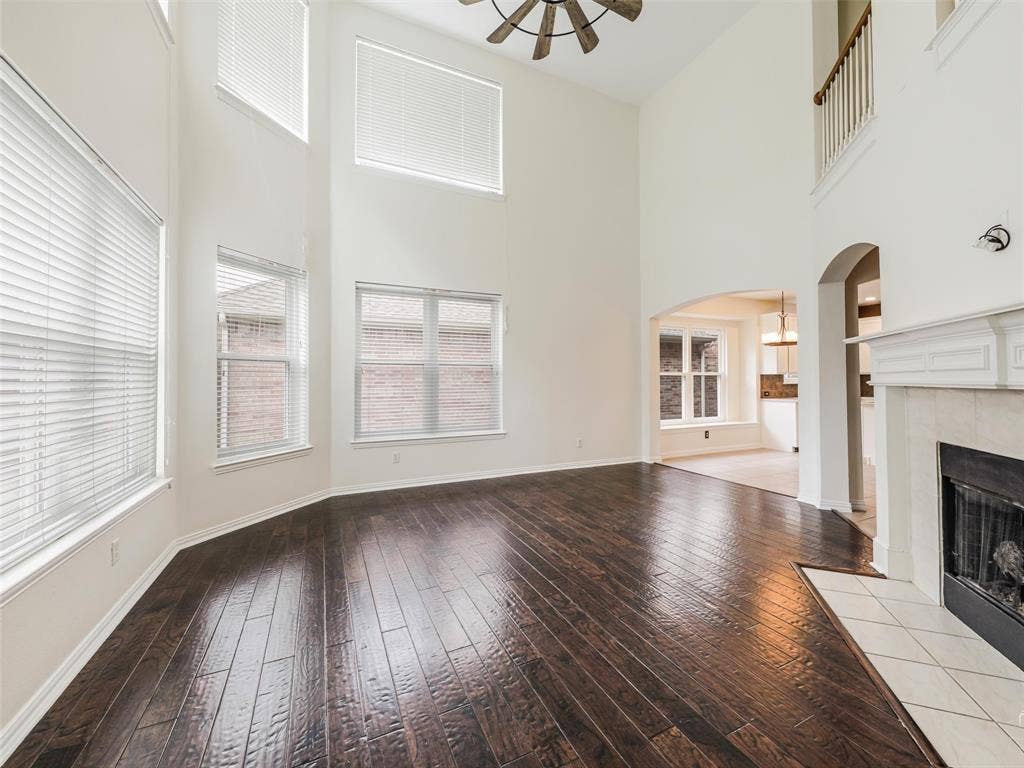 3504 Anita Drive, McKinney, TX 75070 Two-story living area featuring vaulted ceilings, wood-finish flooring, a fireplace with a light-toned surround, an arched entryway, and a balcony overlook