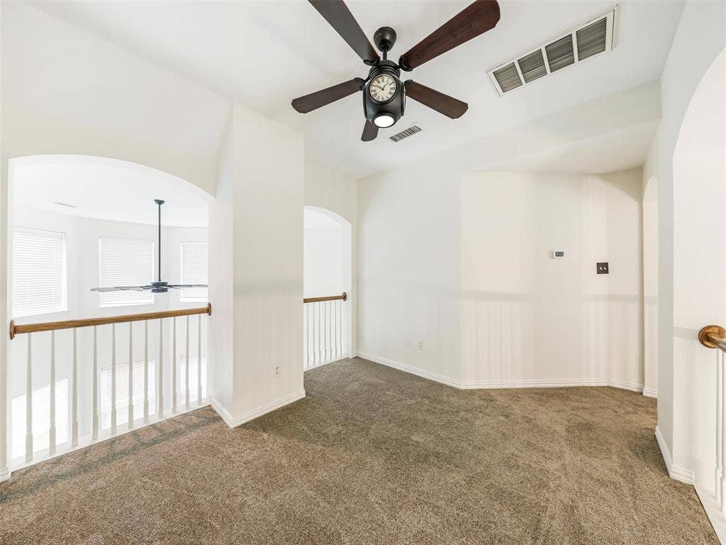 3504 Anita Drive, McKinney, TX 75070 Neutral-toned carpeted flooring, vaulted ceiling with a central multi-blade ceiling fan, and decorative white archways featuring wood-capped white balustrade railings