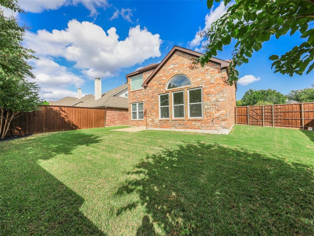 3504 Anita Drive, McKinney, TX 75070 Brick exterior featuring a manicured lawn, wood privacy fencing, arched transom window, and stone-finish rear patio