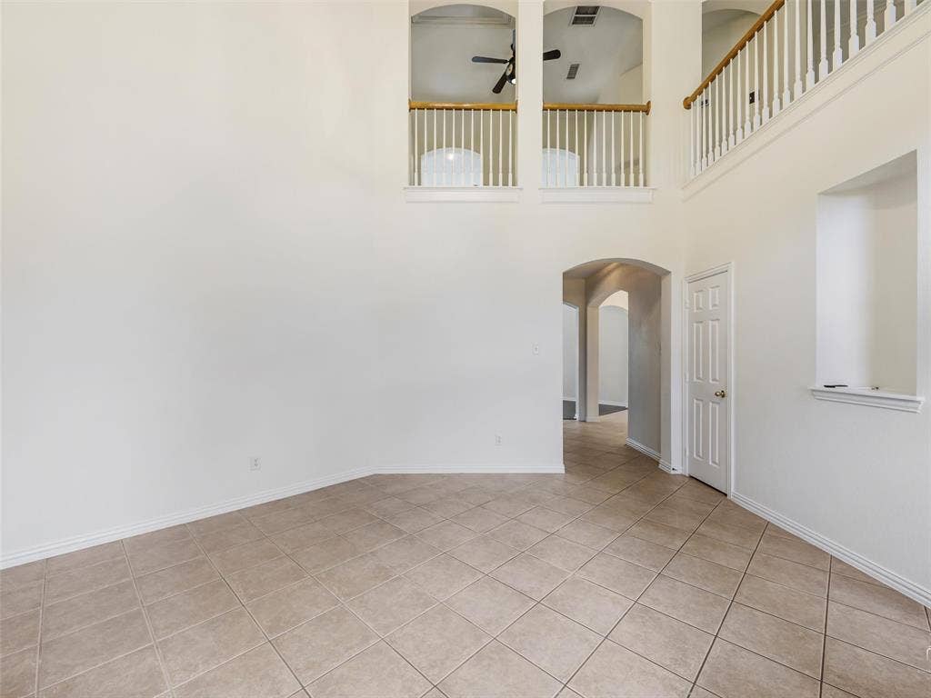3504 Anita Drive, McKinney, TX 75070 Two-story interior space featuring vaulted ceilings, tile flooring, an arched entryway, recessed wall niche, and an elevated landing with a white balustrade and wood-finish railing