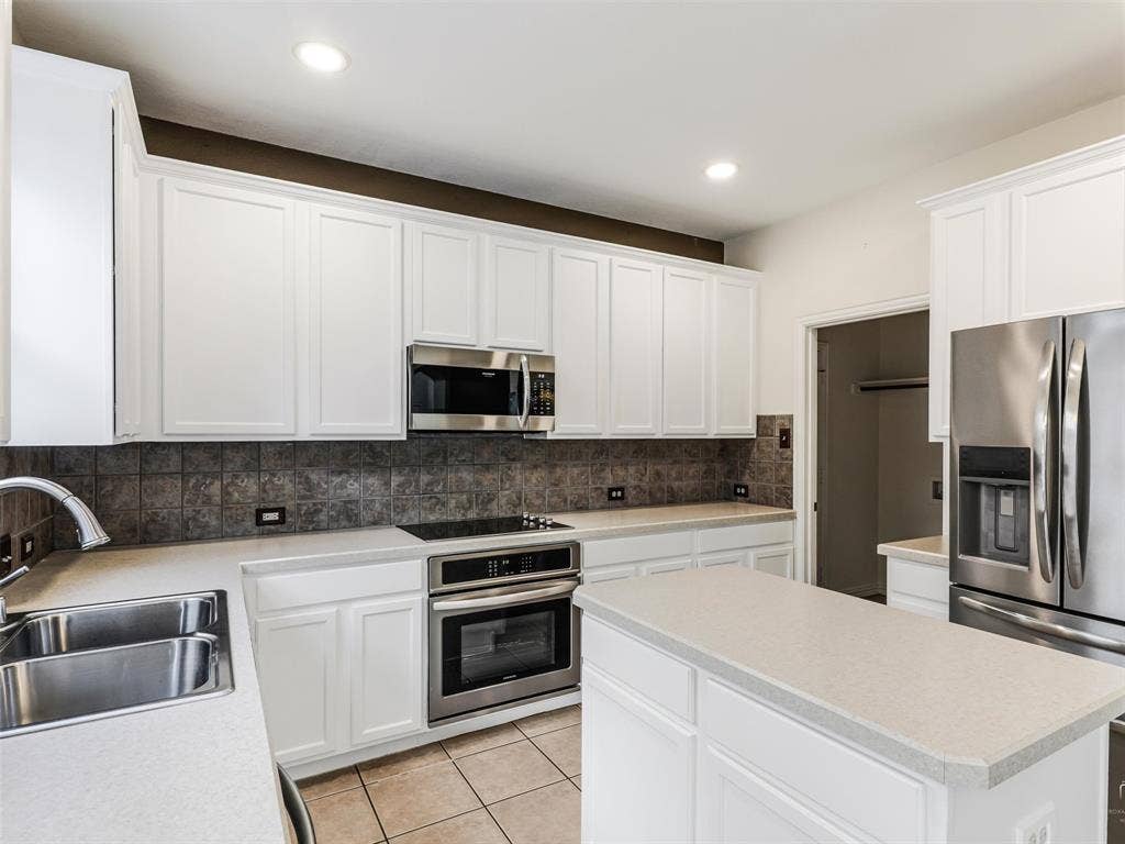 3504 Anita Drive, McKinney, TX 75070 Kitchen featuring white shaker-style cabinetry, stone-finish countertops, stainless steel appliances, ceramic tile backsplash, and tile flooring