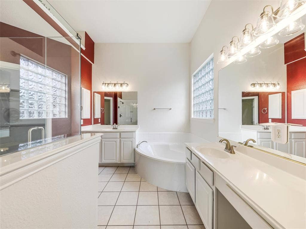 3504 Anita Drive, McKinney, TX 75070 Dual vanity with white cabinetry and solid-surface countertops, soaking tub, glass-enclosed shower, glass block windows, and ceramic tile flooring