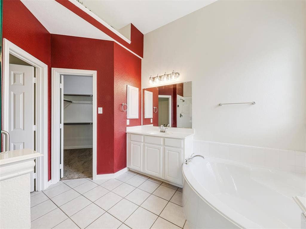 3504 Anita Drive, McKinney, TX 75070 Bathroom featuring a white vanity cabinet with an integrated countertop and sink, wall-mounted mirror, multi-bulb lighting fixture, and a soaking tub
