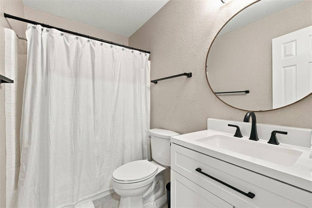813 Chambers Creek Circle, Hewitt, TX 76643 Bathroom featuring a white vanity with matte black hardware, integrated sink, oval wall-mounted mirror, and a combination tub and shower with matte black fixtures