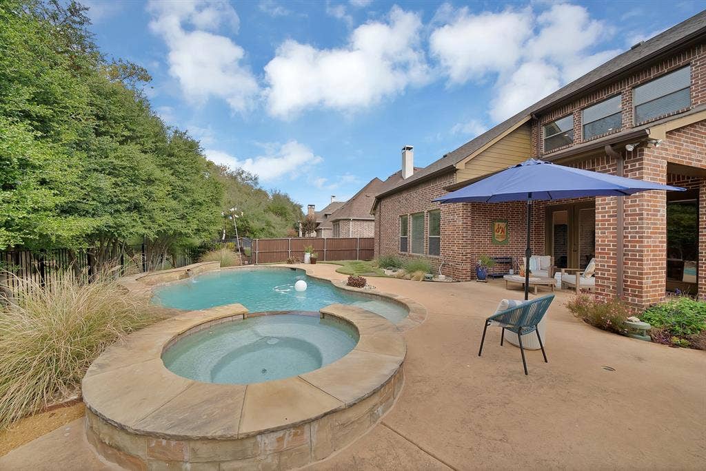 2141 Waterrock Drive, Allen, TX 75013 Brick exterior, inground swimming pool, elevated stone-capped spa, and expansive concrete patio