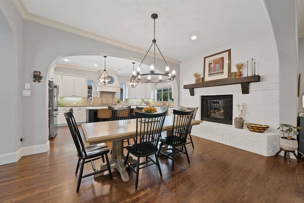 2141 Waterrock Drive, Allen, TX 75013 Dining space featuring wood-finish flooring, a white brick fireplace with a timber mantel, an arched wall opening, and a multi-light wrought iron chandelier