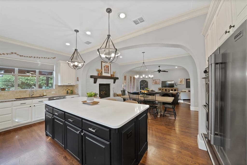 2141 Waterrock Drive, Allen, TX 75013 Kitchen featuring a central island with a solid surface countertop, wood-finish flooring, white and charcoal cabinetry, and dual geometric pendant lighting under arched architectural detailing
