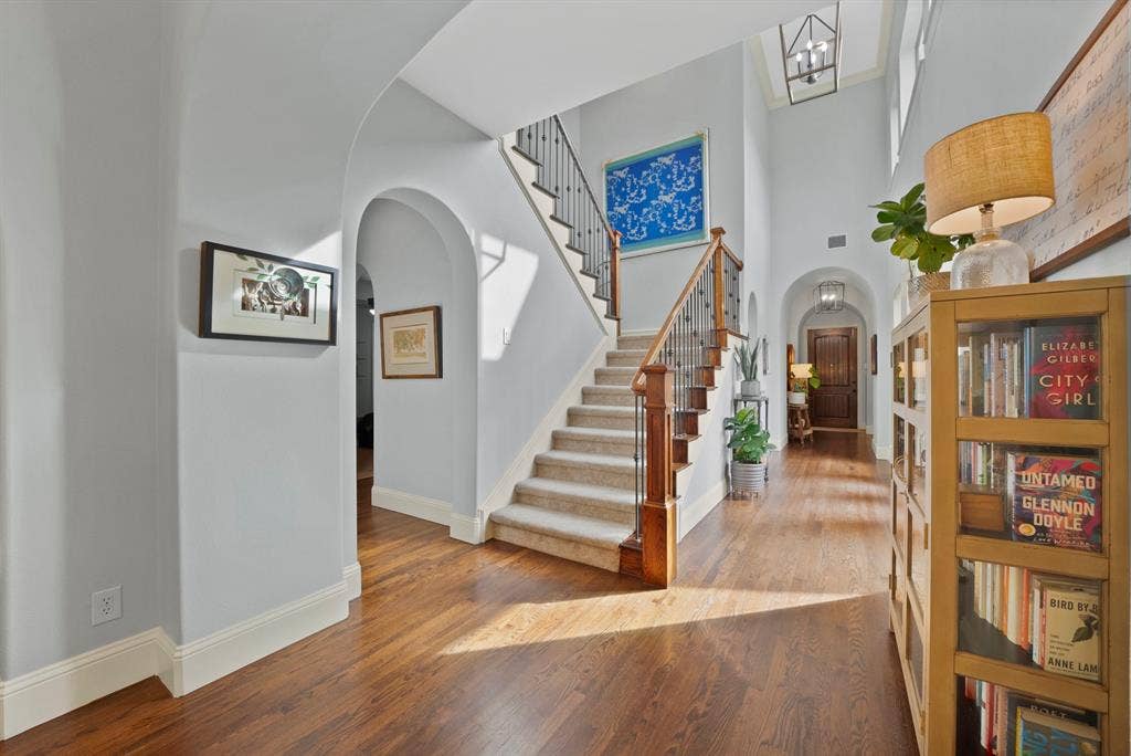 2141 Waterrock Drive, Allen, TX 75013 Foyer featuring arched architectural details, wood-finish flooring, a two-story ceiling, a staircase with decorative metal balusters, and a tiered hanging light fixture