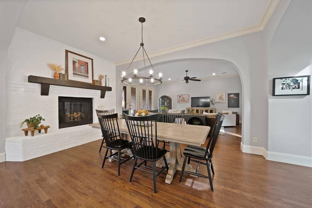 2141 Waterrock Drive, Allen, TX 75013 White brick fireplace featuring a dark wood mantel, wood-finish flooring, architectural arched opening, and an overhead multi-light chandelier