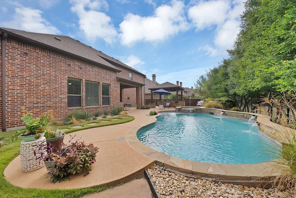 2141 Waterrock Drive, Allen, TX 75013 Brick exterior, expansive concrete patio, in-ground swimming pool with stone-accented water features, attached hot tub, and detached covered patio structure