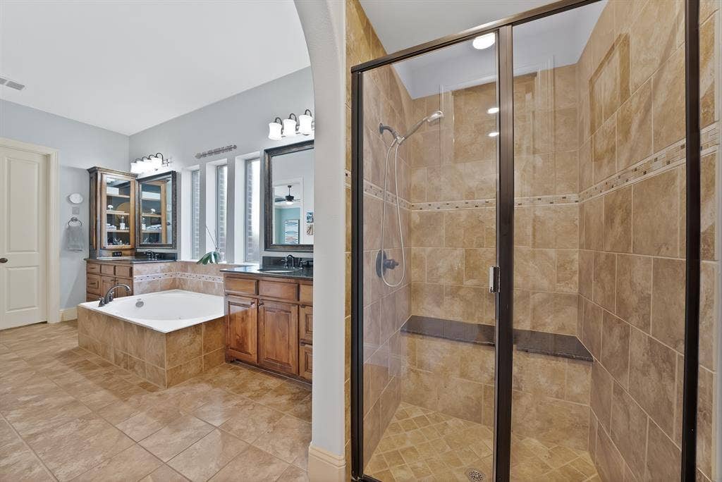 2141 Waterrock Drive, Allen, TX 75013 Bathroom featuring a tiled shower enclosure with a built-in bench, jetted soaking tub, dark wood cabinetry, and multiple light fixtures