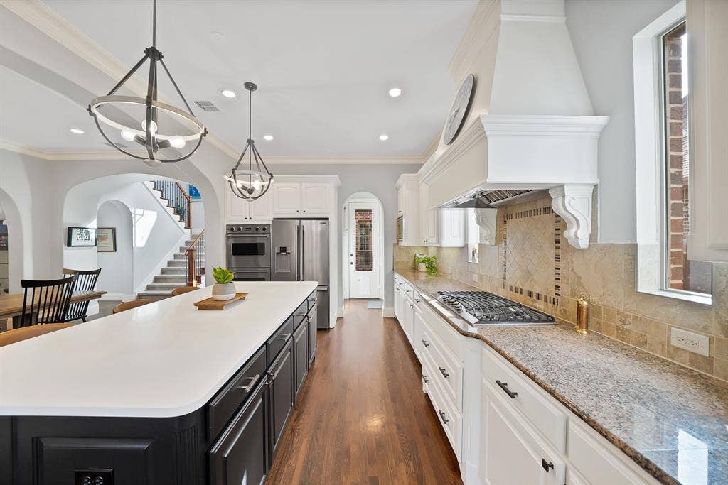 2141 Waterrock Drive, Allen, TX 75013 Kitchen featuring a large central island with solid-surface countertop, custom cabinetry, stainless steel double wall ovens, gas cooktop, and stone tile backsplash