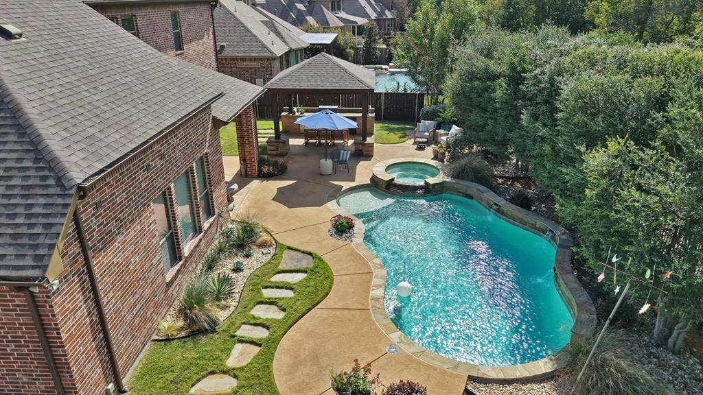 2141 Waterrock Drive, Allen, TX 75013 Backyard featuring a custom swimming pool with integrated spa, concrete patio, covered pavilion, and stone stepping stones set within a manicured lawn