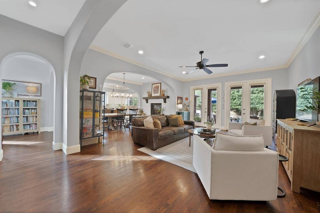 2141 Waterrock Drive, Allen, TX 75013 Open-concept living space featuring wood-finish flooring, recessed lighting, architectural arched doorways, a fireplace with a wood mantel, and multiple sets of glass-paned double doors