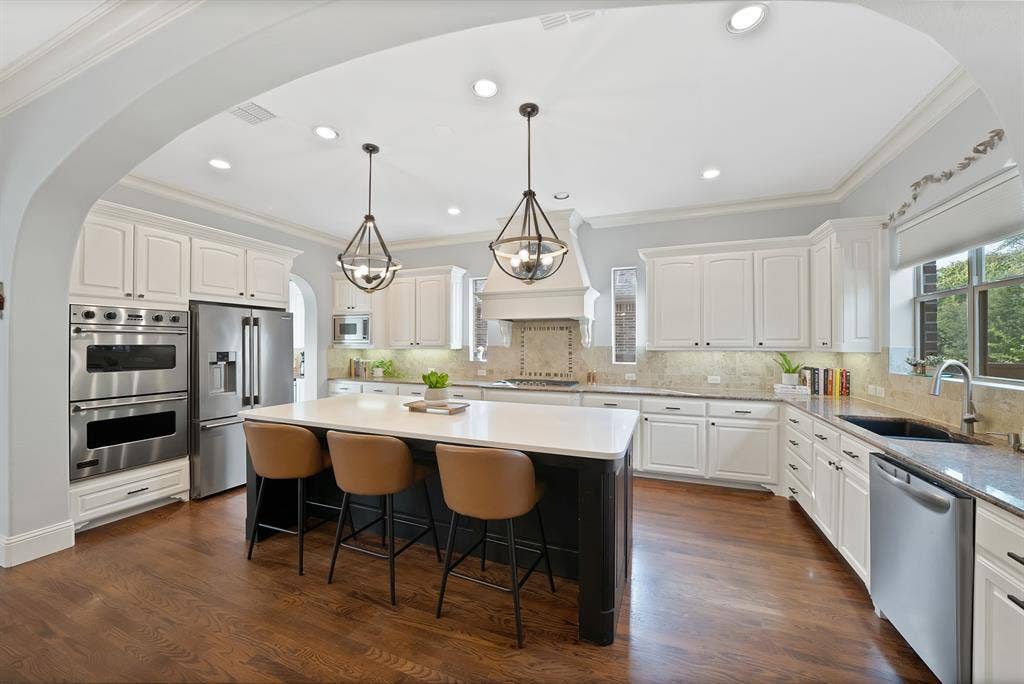 2141 Waterrock Drive, Allen, TX 75013 Kitchen featuring white shaker cabinetry, a contrasting dark central island with a solid surface countertop, wood-finish flooring, stainless steel double wall ovens, and custom pendant lighting