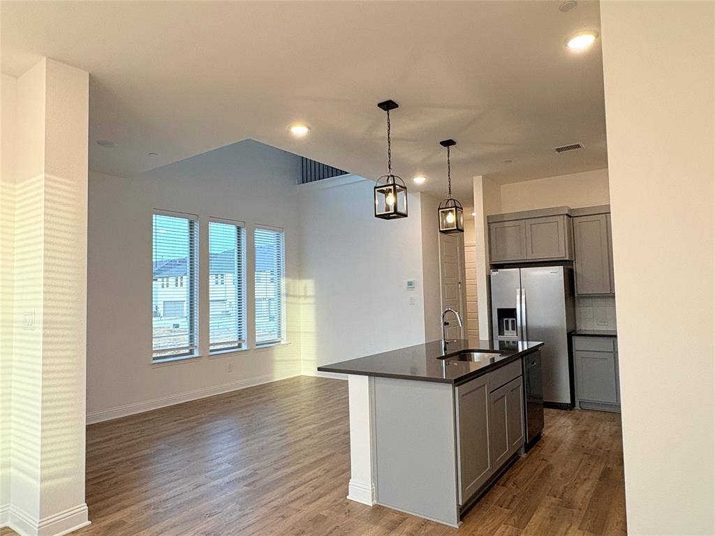 2528 Brunswick Way, Allen, TX 75013 Kitchen featuring grey shaker-style cabinetry, stainless steel appliances, a dark-surface island with an integrated sink, wood-finish flooring, and pendant lighting