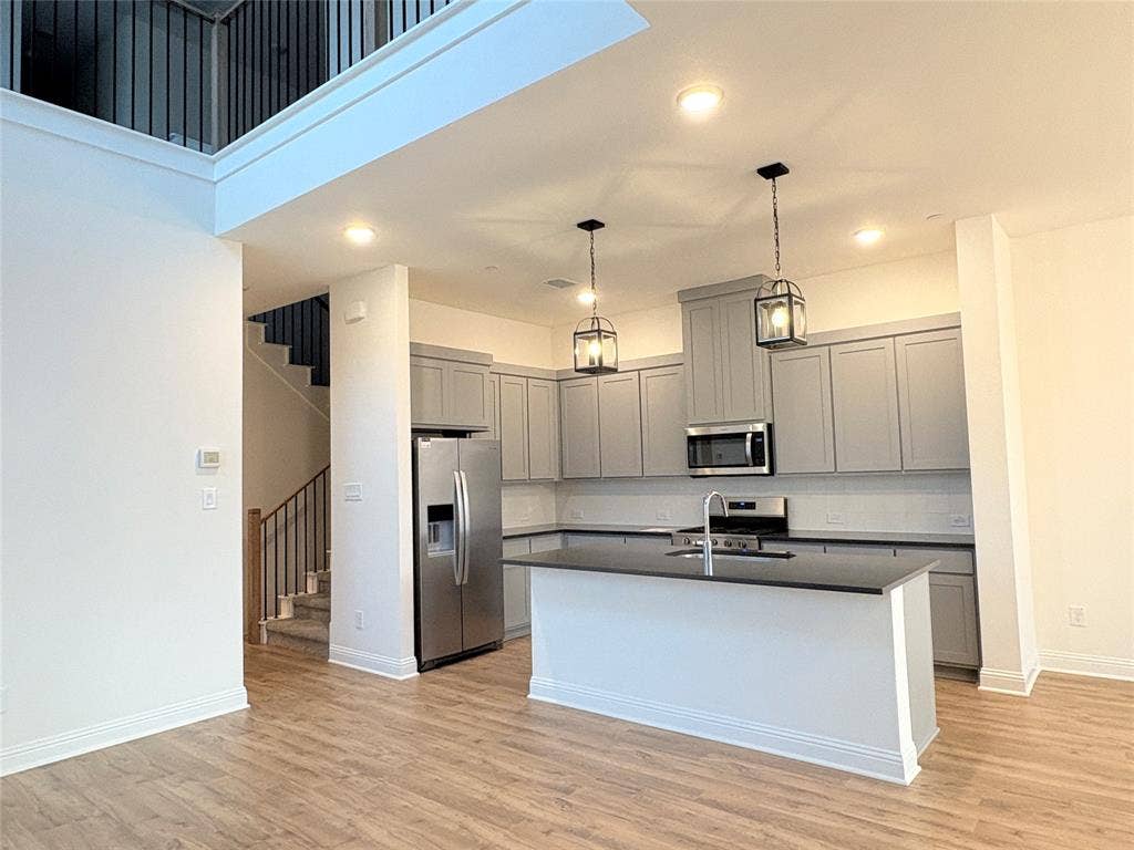 2528 Brunswick Way, Allen, TX 75013 Kitchen featuring grey shaker-style cabinetry, dark stone countertops, an integrated island, stainless steel appliances, and wood-finish flooring