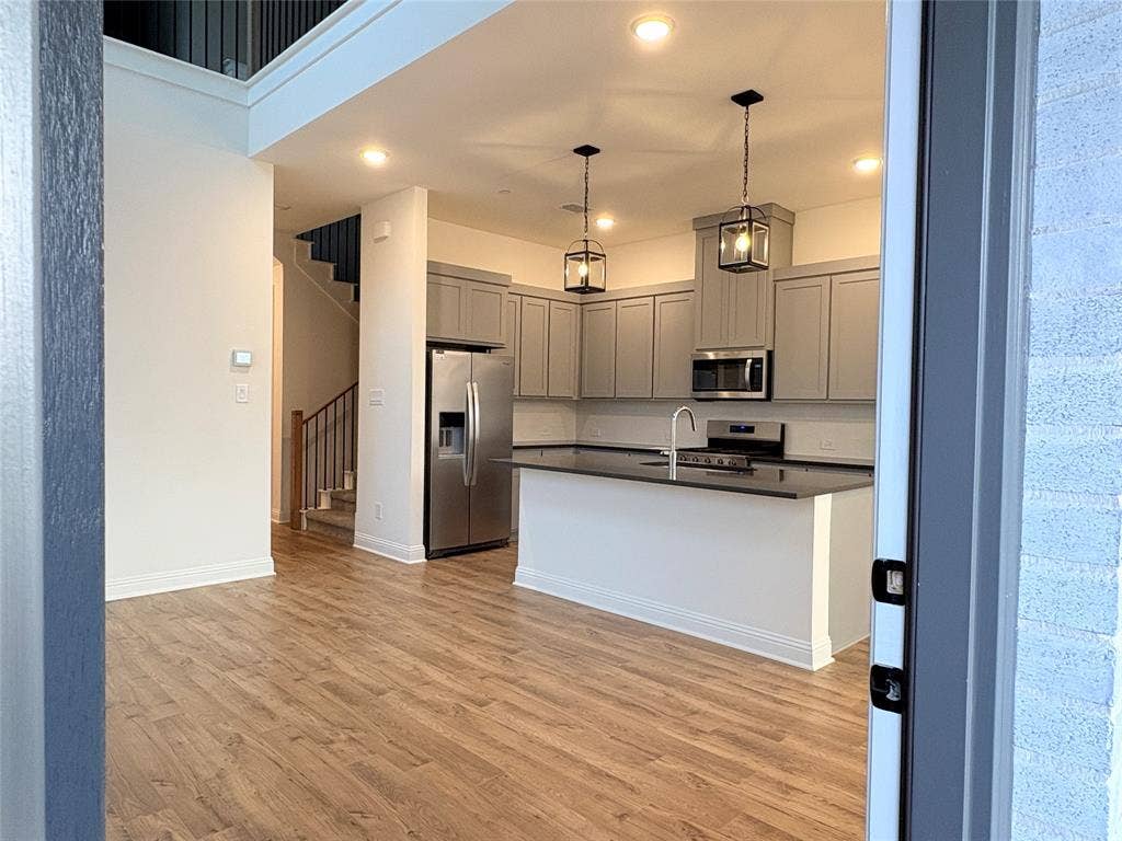 2528 Brunswick Way, Allen, TX 75013 Kitchen featuring cabinetry with a gray finish, stone-surface island, stainless steel appliances, pendant lighting, and wood-finish flooring