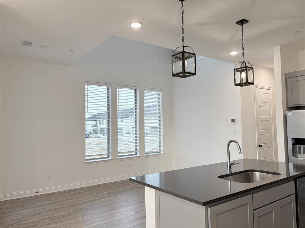 2528 Brunswick Way, Allen, TX 75013 Open-concept kitchen featuring an island with a solid surface countertop, stainless steel undermount sink, shaker-style cabinetry, wood-finish flooring, and pendant lighting