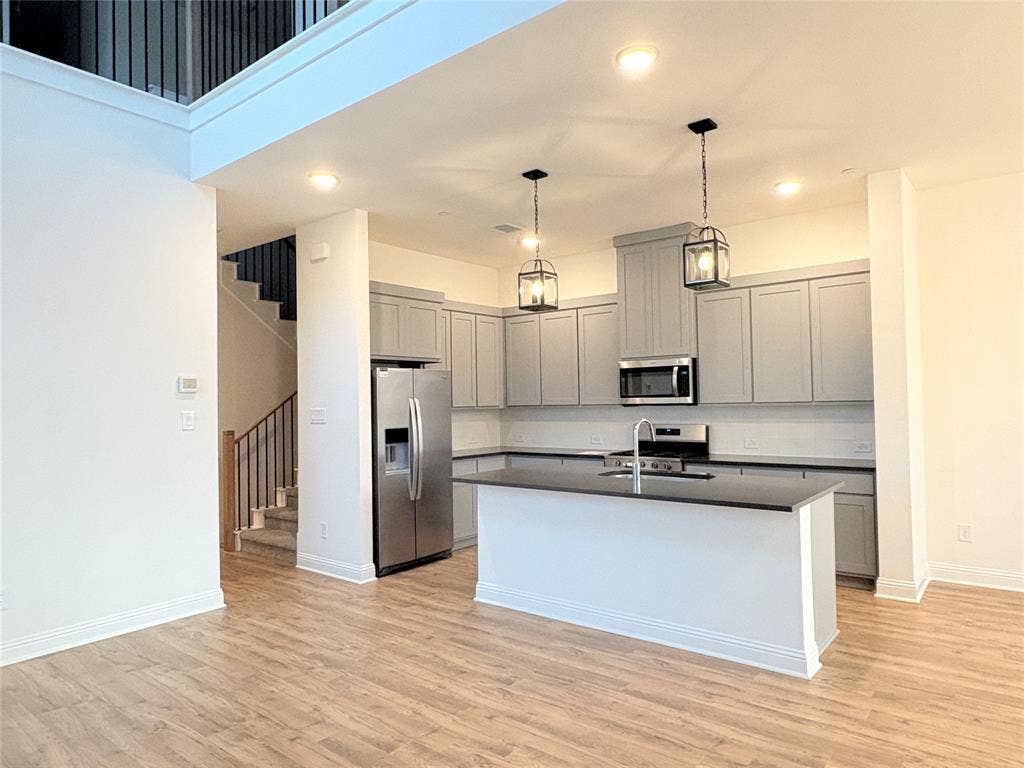2528 Brunswick Way, Allen, TX 75013 Kitchen featuring gray shaker-style cabinetry, stainless steel appliances, a center island with a stone-finish countertop, wood-finish flooring, and pendant lighting