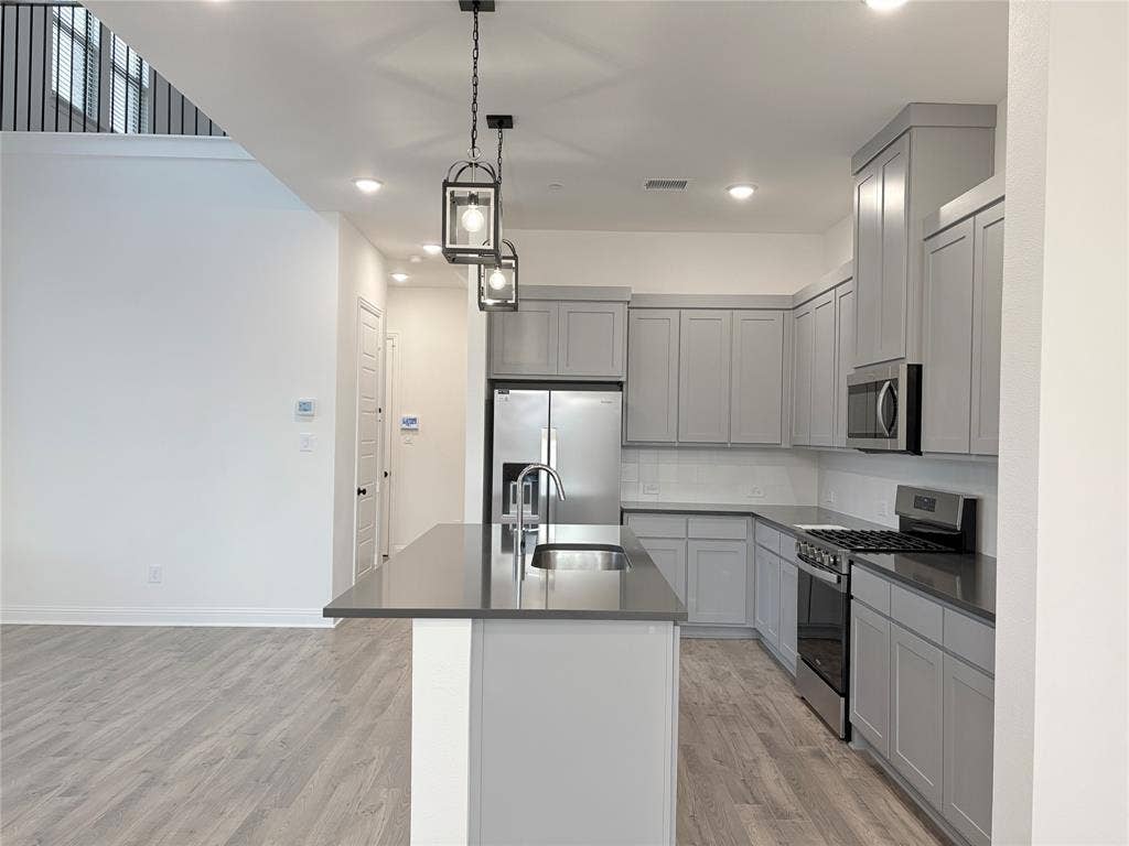 2528 Brunswick Way, Allen, TX 75013 Kitchen featuring Shaker-style cabinetry, a central island with a stainless steel sink, solid-surface countertops, wood-finish flooring, and pendant lighting