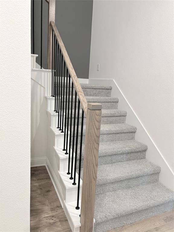 2528 Brunswick Way, Allen, TX 75013 Staircase featuring a light-toned wood handrail, vertical matte black metal balusters, white risers, and neutral-toned carpeting